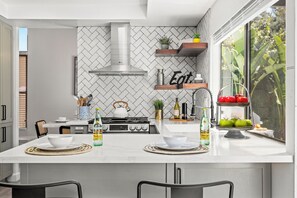 A modern kitchen with a central island, white herringbone backsplash, and a window with a view of greenery.