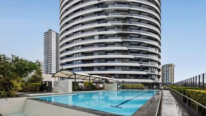 A modern hotel with a curved facade, a swimming pool, and a covered outdoor area. - Luxury Apartment - Oracle Broadbeach  (Broadbeach)