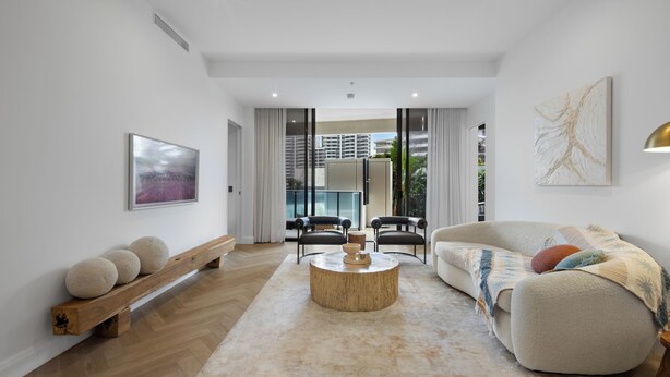 A modern living room with a round wooden coffee table, a beige sofa, and a bench with decorative balls. - Luxury Apartment - Oracle Broadbeach  (Broadbeach)