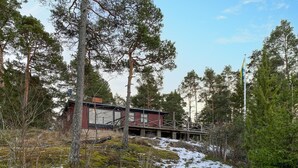 A cabin with a red exterior, surrounded by tall pine trees and snow patches. - 3 bedroom amazing home in Yxlan (Yxlan)