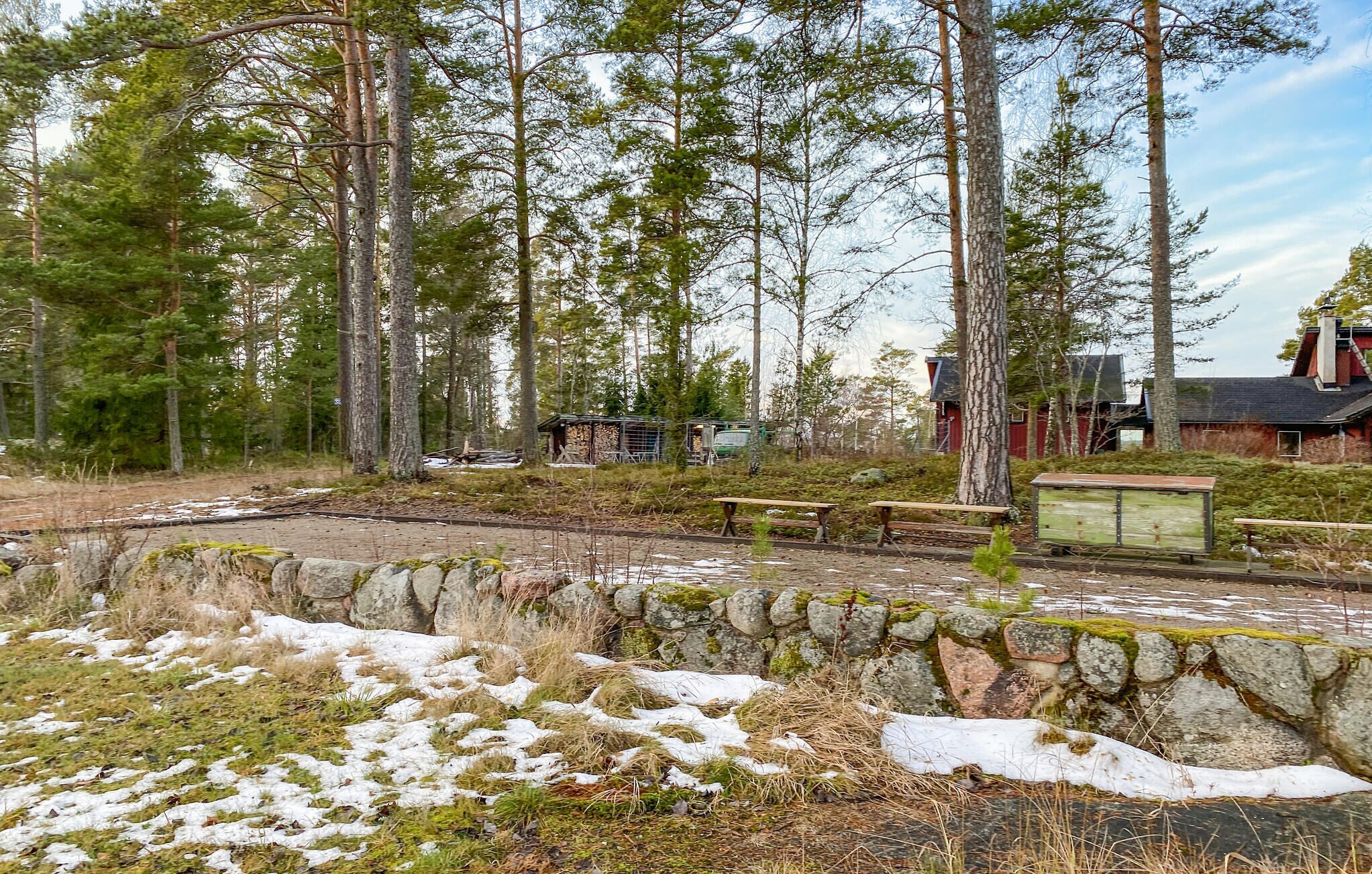 Viehättävä, maalaishenkinen mökki, jonka ympärillä kohoaa korkeita mäntyjä, ja sen lähellä on kivimuuri sekä piknikpöytä.