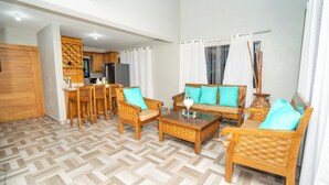 Un salon avec un parquet en chevrons, des meubles en bois et une cuisine à l’arrière-plan.