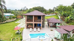 Une maison à deux étages avec une piscine, un espace salon extérieur et un jardin clôturé.