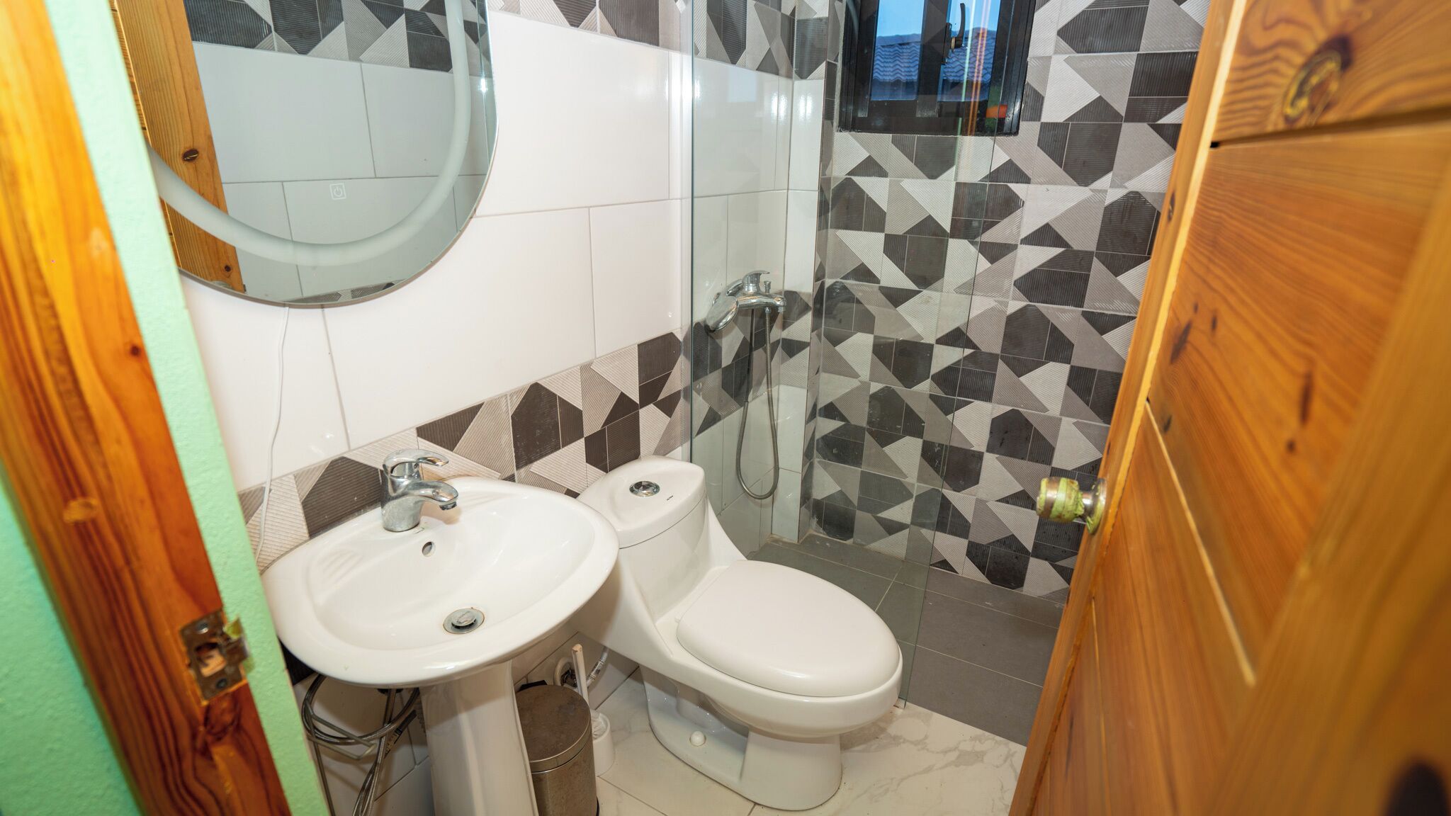 A bathroom with a white sink, a toilet, and a shower. The walls have a geometric tile pattern.