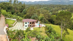 Une maison à deux étages avec une piscine, entourée d’une végétation luxuriante et avec des montagnes en toile de fond.