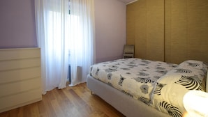 A bedroom with a bed, a wooden wardrobe, a window with sheer curtains, and a wall-mounted light fixture. - 1 bedroom cozy apartment in Roma (Roma)