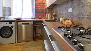 A kitchen with a washing machine, a sink, a stove, and a window with curtains. - 1 bedroom cozy apartment in Roma (Roma)