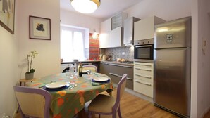 A kitchen with a dining table set for two, a refrigerator, and a window with a view. - 1 bedroom cozy apartment in Roma (Roma)