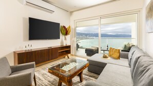 A modern living room with a flat-screen TV, a wooden entertainment unit, a glass coffee table, and a grey sofa. - Wake Up to Paradise – Stunning 2BR Condo Right on the Beach (Puerto Vallarta)