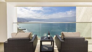 A balcony with wicker furniture, a glass table, and a bottle of wine. - Wake Up to Paradise – Stunning 2BR Condo Right on the Beach (Puerto Vallarta)