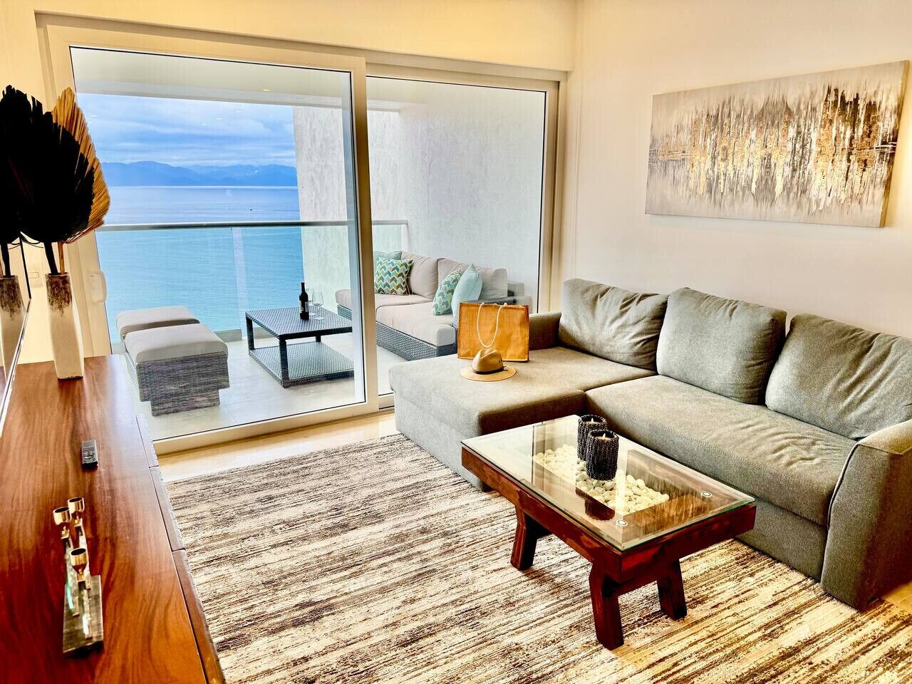 A modern living room with a sofa, coffee table, and a view of the sea through a sliding glass door.