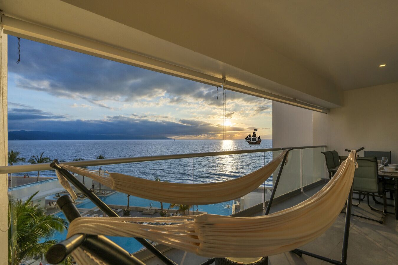 Un balcon avec un hamac, une piscine et une vue sur l’océan, avec un navire à l’horizon.