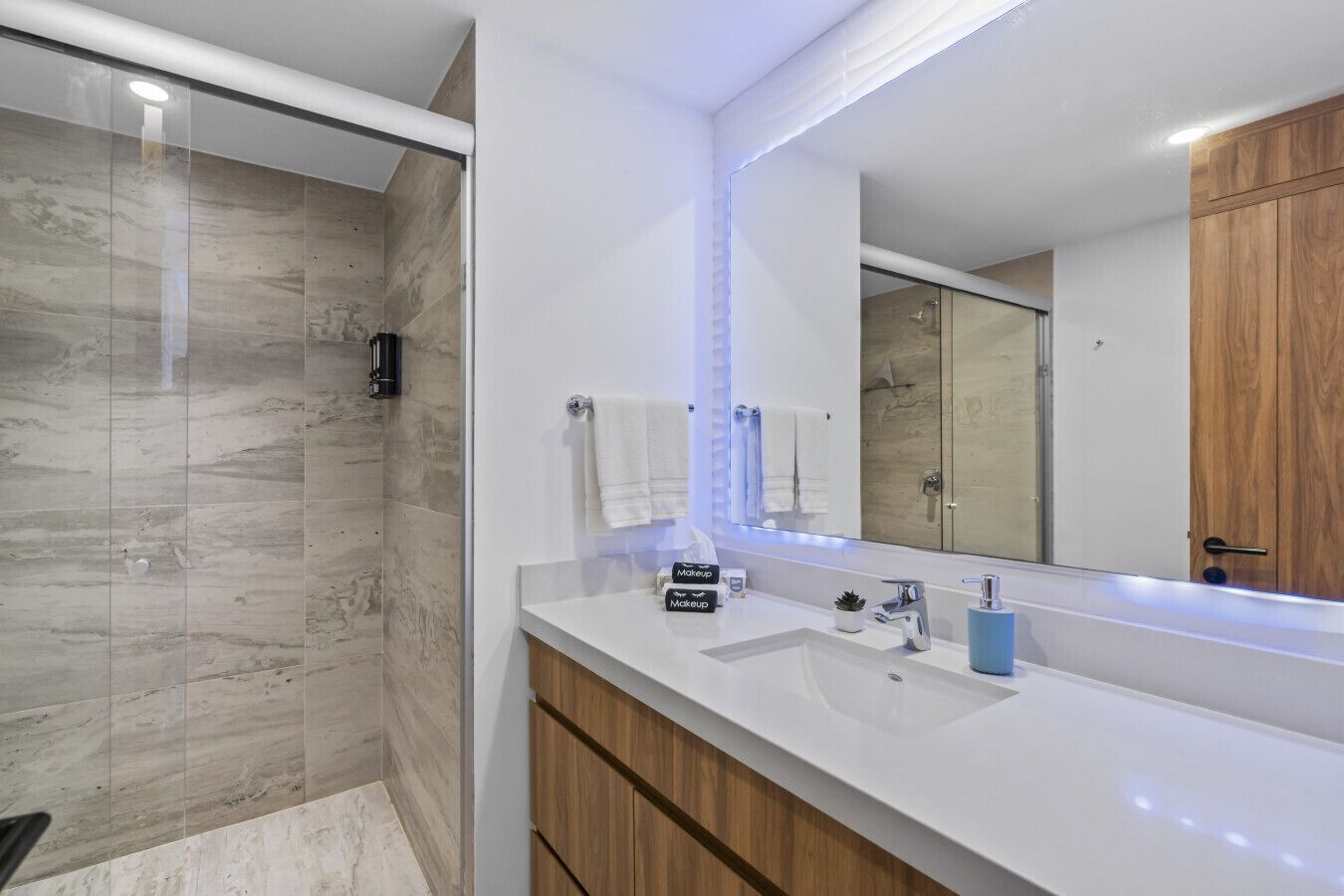 Een moderne badkamer met een douchecabine van glas, een wit wastafelmeubel met spiegel en houten kasten.