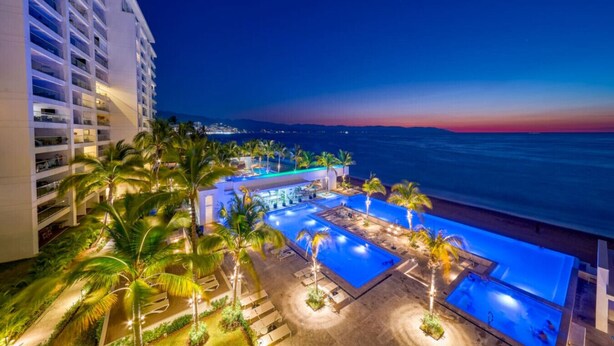 A hotel with multiple swimming pools, palm trees, and a view of the ocean at sunset. - Oceanfront Luxury + FREE Daily Breakfast Harbor171 (Puerto Vallarta)