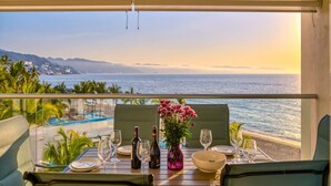 A dining table set with wine glasses, bottles, and a vase of flowers, overlooking a pool and ocean view. - Oceanfront Luxury + FREE Daily Breakfast Harbor171 (Puerto Vallarta)