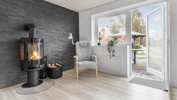 A modern interior with a wood-burning stove, a comfortable chair, and a view of the outdoors through large windows.