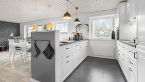 A modern kitchen with white cabinets, a central island, pendant lights, and a view of the outdoors through large windows.