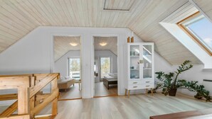 A spacious attic bedroom with a sloped ceiling, wooden flooring, a built-in wardrobe, and a large window.