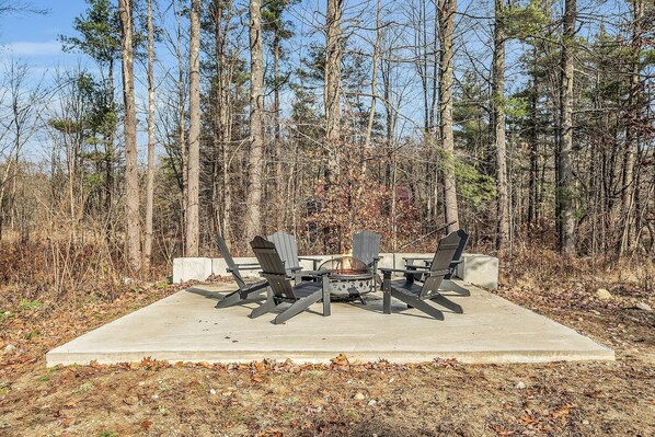 An outdoor seating area with four Adirondack chairs and a fire pit, surrounded by a forest. - NEW! Relax&Play: HotTub/FirePit/Game Room Paradise (Tamworth)