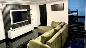 A modern living room with a sectional sofa, a flat-screen TV mounted on a white console, and a staircase leading to an outdoor area. - Villa Bijou in Abidjan (Abidjan)