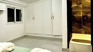 A hotel room with a bed, a robe, a remote control, and a shower with a glass door. - Villa Bijou in Abidjan (Abidjan)