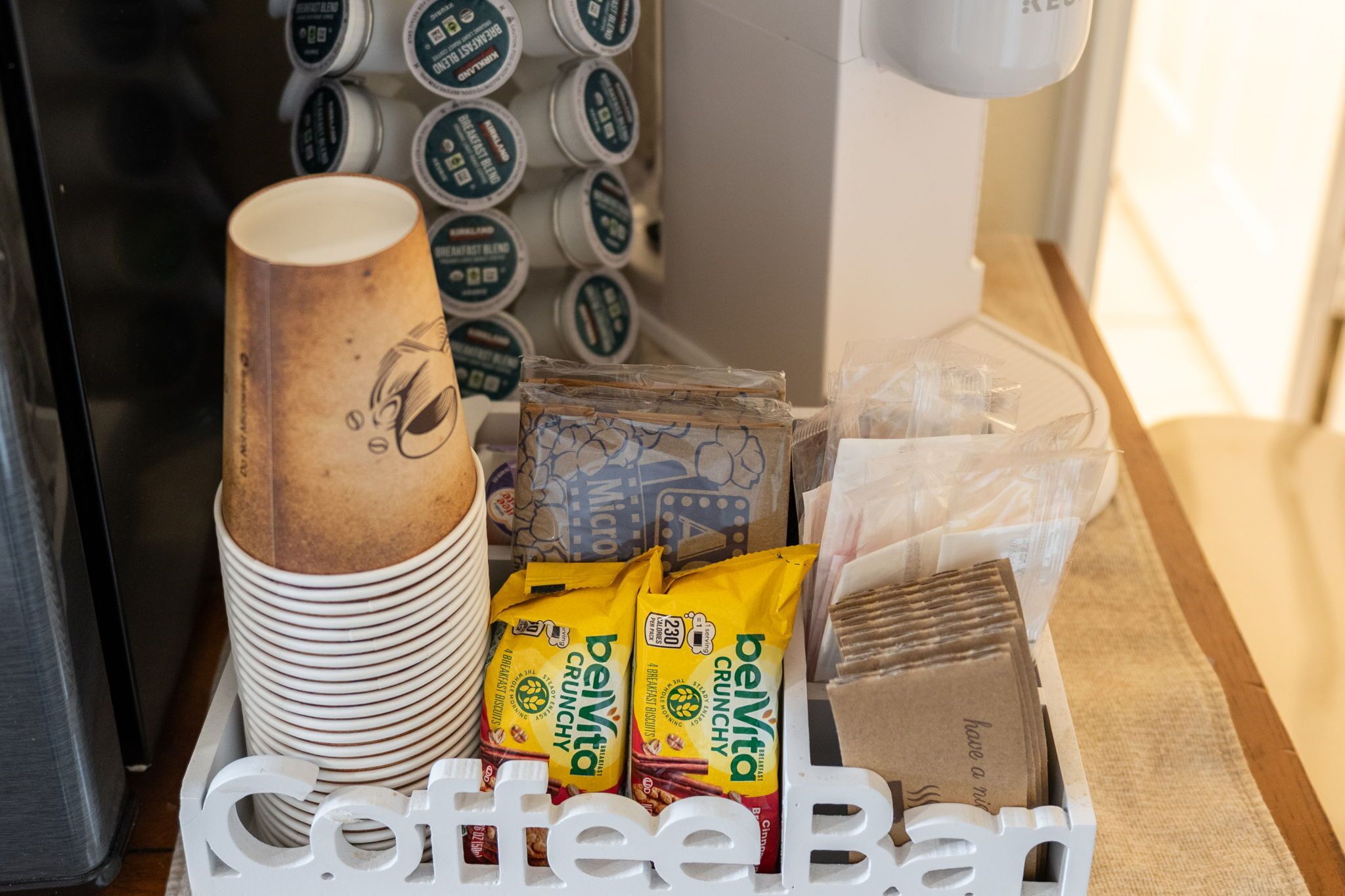 Una cafeteria amb piles de gots de paper, bosses de cereal Belvita Crunchy i una màquina de cafè.
