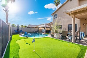 A backyard with a swimming pool, artificial grass, lounge chairs, and a patio area. - Suite Retreat - Private Courtyard, Pool, Hot Tub, Cabana, Putting Green (Peoria)