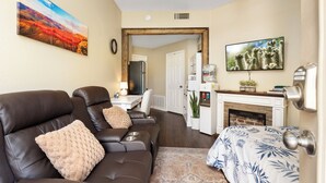 A living room with a leather sofa, a patterned rug, a fireplace, and a television. - Private Guest Suite - Pool, Hot Tub, Cabana, Courtyard & Putting Green (Peoria)