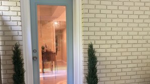 Een deur met een geëtste glazen ruit, omgeven door twee potplanten en een deurmat waarop de tekst 