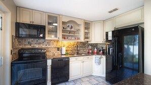 A kitchen with white cabinets, a black refrigerator, and a microwave. There is a sink and a stove. - Pool + Tennis/B-Ball Courts + Game Room + Mins to Disney! (Kissimmee)