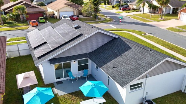 A residential house with a garage, solar panels, a covered patio with chairs and umbrellas, and a street view. - Pool + Tennis/B-Ball Courts + Game Room + Mins to Disney! (Kissimmee)