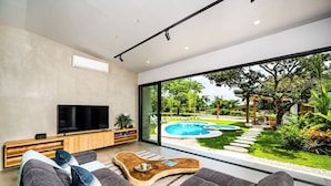 A modern living room with a large TV, comfortable seating, a wooden coffee table, and a view of a swimming pool and garden. - Luxury Modern Escape in Hacienda Pinilla: Beach Club Access & Endless Adventure! (Pinilla)
