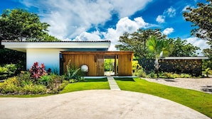 A modern house with a concrete driveway, a wooden structure, and lush greenery. - Luxury Modern Escape in Hacienda Pinilla: Beach Club Access & Endless Adventure! (Pinilla)