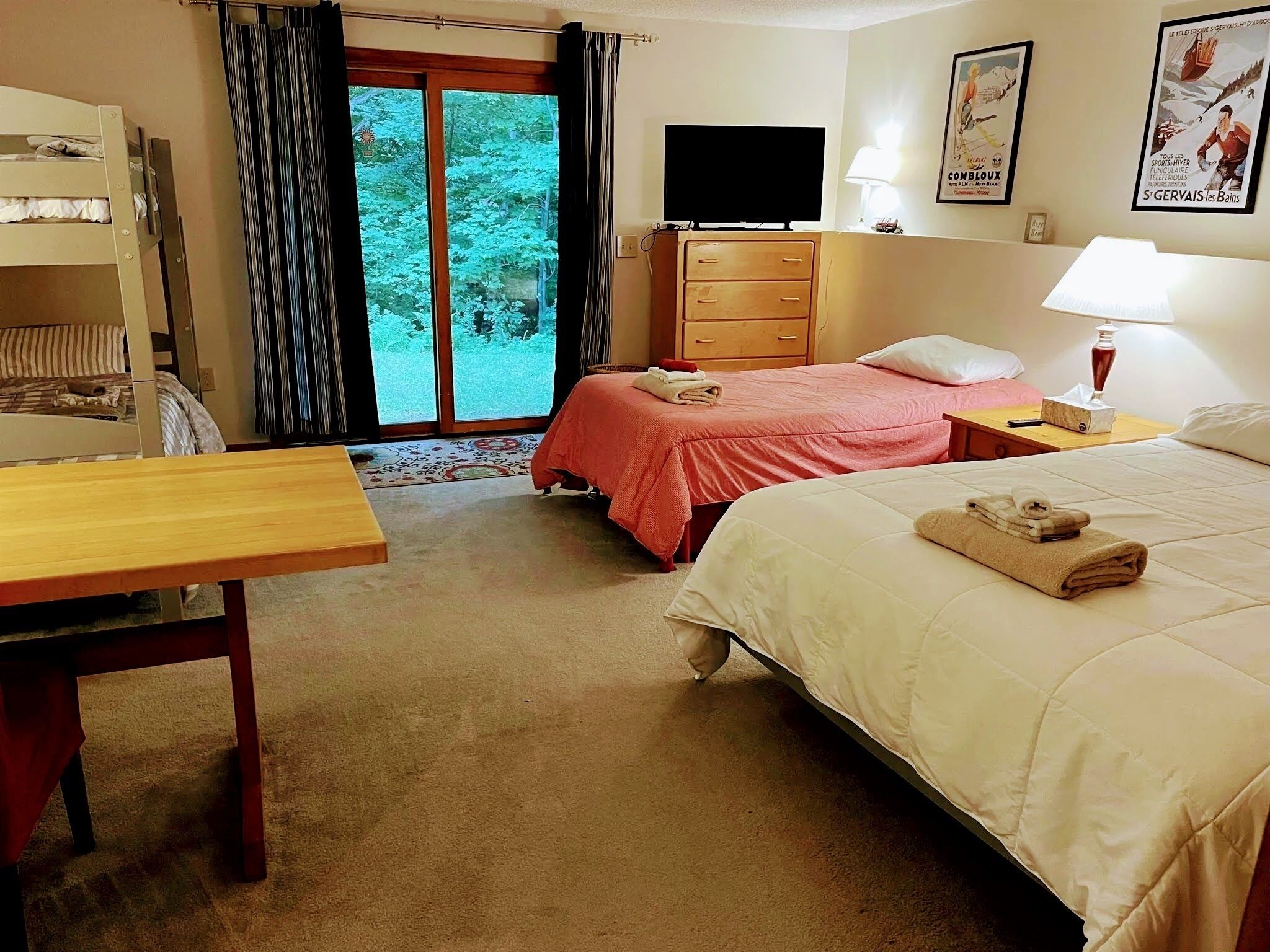 A hotel room with two beds, a desk, a television, and a window with curtains.