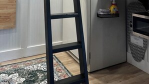 Eine Küche mit integriertem Kühlschrank, einer Leiter, einem Regal mit Küchenutensilien und einem gemusterten Teppich.