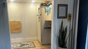 Eine moderne Küche mit Kühlschrank, einem Holzkasten und einer Arbeitsfläche. Eine Topfpflanze und ein Fenster mit Vorhängen sind ebenfalls vorhanden.