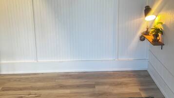 Une pièce avec un tableau représentant un paysage, encadré, un plancher en bois et un tapis à motifs.
