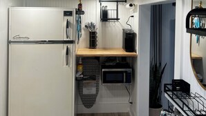 Eine kleine Küche mit Kühlschrank, Mikrowelle und Spüle. Ein Holzregal und eine kleine Arbeitsplatte sind vorhanden.