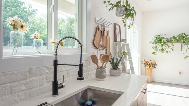 A modern kitchen with a white brick backsplash, a stainless steel sink, and wooden utensils hanging on the wall. - Romantic Farm House (Springfield)