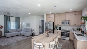 A modern kitchen with stainless steel appliances, a dining area with a wooden table and chairs, and a living area with a sofa and a coffee table. - Romantic Farm House (Springfield)