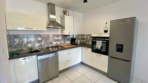 Una cocina moderna con armarios blancos, una estufa de acero inoxidable, un horno empotrado y un refrigerador.