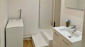 Un baño pequeño con un lavamanos, espejo y ducha blancos.