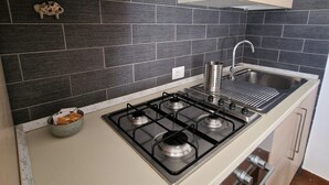 A kitchen with a gas stove, stainless steel sink, and light wooden cabinets. - Apartment 5 min from Airport, Self Check-in h24, Private Garden, Wi-Fi, A/C, TV (Rome Fiumicino)