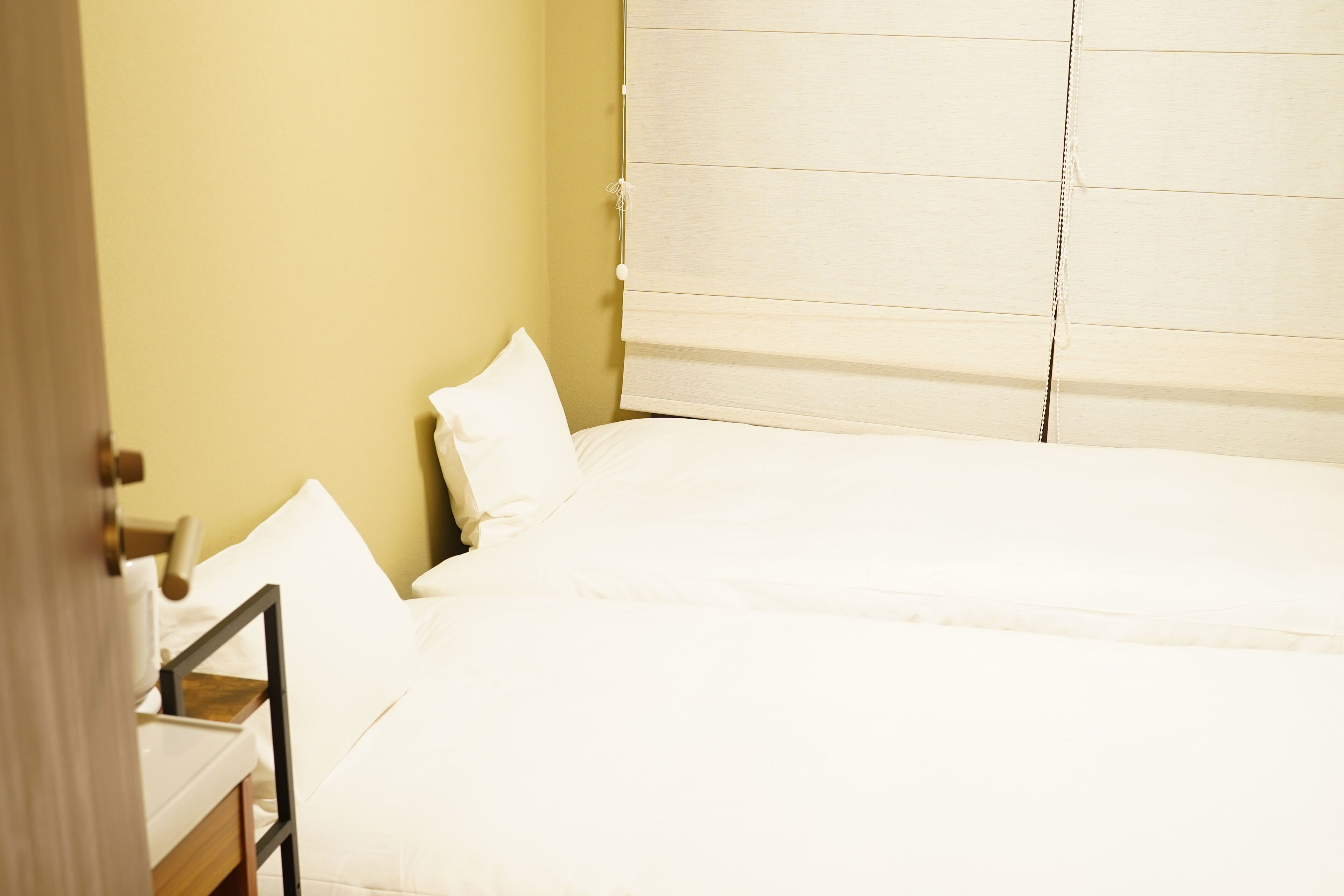 A room with a bed, a bedside table, and a window with blinds.