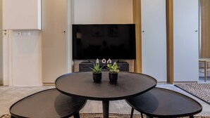 A modern living room with a round black table, two black benches, and two potted plants. A flat-screen TV is mounted on the wall above the table. - Wonderful Apartment 1br4p (Paris)