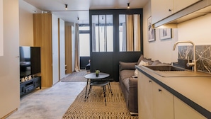 A modern living room with a sofa, TV, and kitchen area with a sink and countertop. - Wonderful Apartment 1br4p (Paris)
