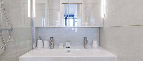 A modern bathroom with a large sink, two faucets, and a glass shower enclosure.