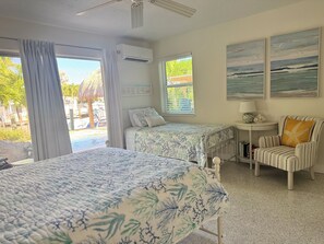 A room with two beds, a chair, a small table, and artwork on the walls.