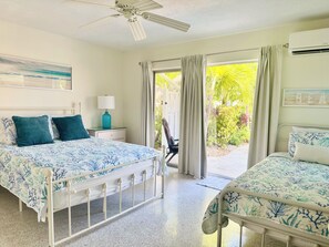 Une chambre avec deux lits, un ventilateur de plafond, une fenêtre avec des rideaux et un appareil de climatisation.