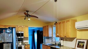 Une cuisine avec des meubles de rangement en bois, un réfrigérateur, une cuisinière, un ventilateur de plafond et une table à manger avec des chaises.